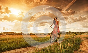 Beautiful woman with old bike in a wheat field