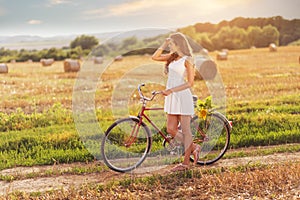 Beautiful woman with old bike in a wheat field