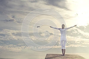 Beautiful woman with open arms meditating in front of a spectacular sky