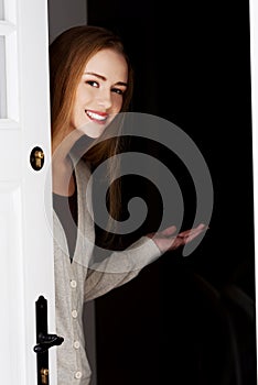 Beautiful woman is opening door and inviting to come in.