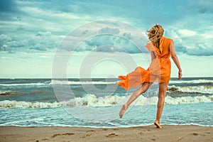 Krásna žena v oranžový šaty lietanie vlak tanec naboso na mokrý piesok na útočiť more 