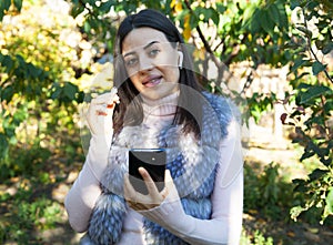 Beautiful woman outdoors, has a wireless earphones in her ears. Hand phone