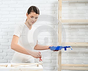 Beautiful woman painting old furniture with white color