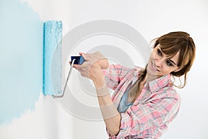 Beautiful woman painting wall with paint roller