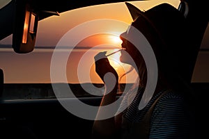 Beautiful woman paints her lips in the car .The evening sunset on the promenade