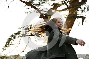 Beautiful woman in the park. girl raising her arms up smiling happy. Joyful young woman is spinning in spring park
