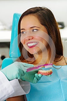 Beautiful woman patient smiling while the doctor is brushing a fake dental plaque in a dentist`s office