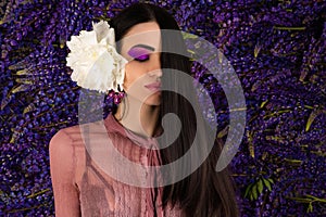 Beautiful woman with peony in hair on background lupine flowers