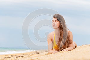 Beautiful woman with perfect body lies on sandy beach, wearing yellow bikini, sunbathing at beach resort, enjoying