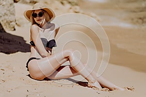 Beautiful woman with perfect body lying down on the beach, wearing stylish hat, tanning on a beach resort, enjoying summer vacatio