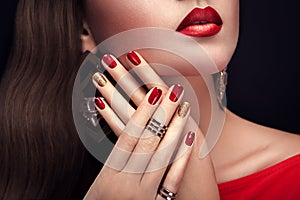 Beautiful woman with perfect make-up and red and golden manicure wearing jewellery