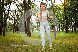 A beautiful woman performs an exercise outdoor. Grass, park, sports workout. Fitness. An expander. Sports equipment