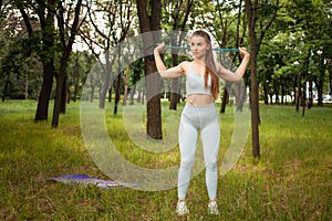 A beautiful woman performs an exercise outdoor. Grass, park, sports workout. Fitness. An expander. Sports equipment