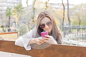 Beautiful woman with phone sitting on bench in the park.