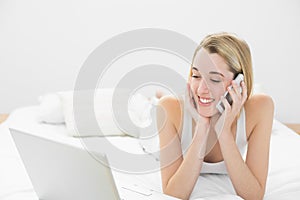 Beautiful woman phoning while lying on her bed using her notebook