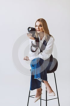 A beautiful woman photographer in a denim casual outfit and a white blouse with voluminous sleeves with a camera in her hands.