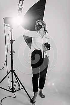A beautiful woman photographer in a protective mask works in a professional photo studio among the lighting equipment. Hobby