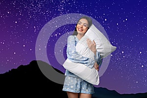 Beautiful woman with pillow, mountains under starry sky on background. Bedtime