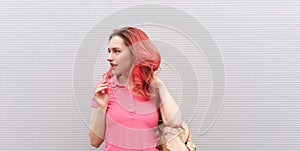 beautiful woman with pink colored hairs and neon sunglasses standing over grey wall. Flying hairstyle