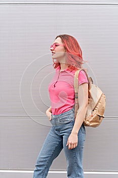 beautiful woman with pink colored hairs and neon sunglasses standing over grey wall. Flying hairstyle