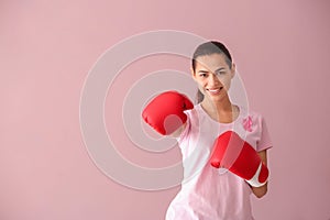 Beautiful woman with pink ribbon and boxing gloves on color background. Breast cancer concept