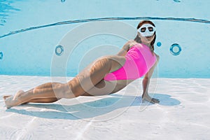 Beautiful woman with pink swimsuit posing underwater in swemming pool