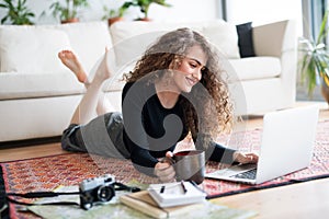 Beautiful woman planning summer vacation abroad, going on trip alone. Lying on floor, working on itinerary on laptop. photo