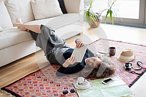 Beautiful woman planning summer vacation abroad, going on trip alone. Lying on floor, working on itinerary on tablet. photo