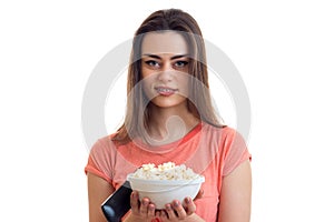 Beautiful woman with a plate of pop corn and remote control looks into the camera and smiling