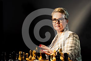 Beautiful woman playing chess on dark background. Old film effect added in postproduction