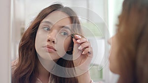 Beautiful woman plucking eyebrows with tweezers in mirror at bathroom