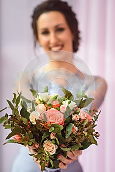 Beautiful woman in a plum dress holding a bouquet of roses and smiling lloking at camera, focus on flowers. photo