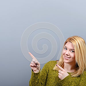 Beautiful woman pointing to blank area against  gray background