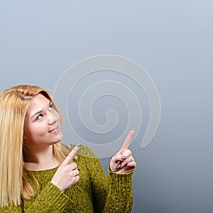 Beautiful woman pointing to blank area against  gray background