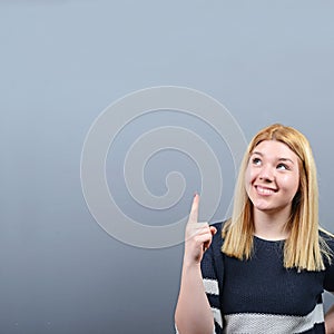 Beautiful woman pointing to blank area against  gray background