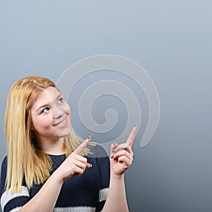 Beautiful woman pointing to blank area against  gray background