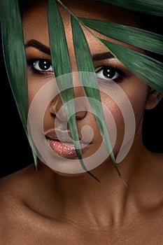 Beautiful woman portrait on black background. Young afro girl posing with green leaves and closed eyes. Gorgeous make up.