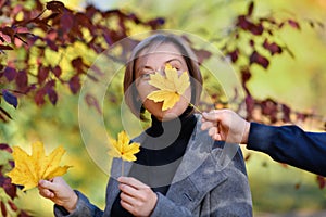 Beautiful woman portrait, she holds a yellow leaf and laughs, the other hand covers her face with a maple leaf, posing in autumn
