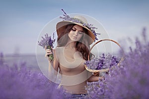 Beautiful woman portrait in lavender field  in Provence. Attractive girl with long curly hair in straw hat  holding violet flowers