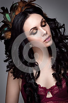 Beautiful woman portrait. Young lady posing on grey background with feathers in hair.