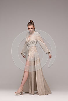 A beautiful woman poses in growth in a delicately silver or golden long dress. photo