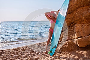Beautiful woman posing in swimsuit and hat on beach. Surfing sport, adventure time and holiday trip idea, copy space