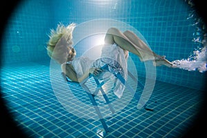 Beautiful woman posing underwater on the chair in white dress