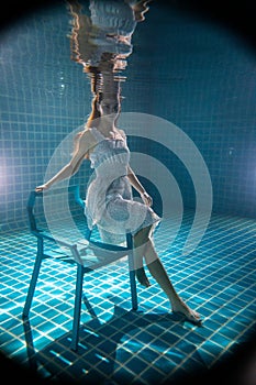 Beautiful woman posing underwater on the chair in white dress