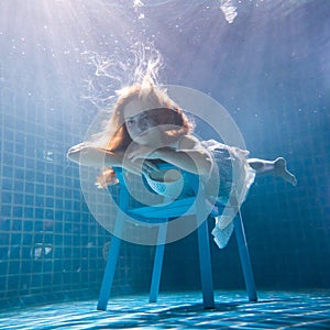 Beautiful woman posing underwater on the chair in white dress