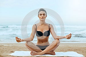 Beautiful woman practices yoga and meditates in the lotus position on th ebeach