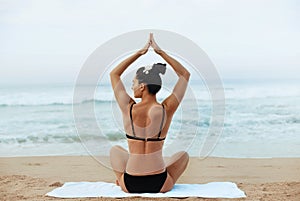 Beautiful woman practices yoga and meditates in the lotus position on th ebeach.