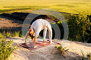 Beautiful woman practicing Wheel yoga asana pose on top of rock background of beautiful landscape