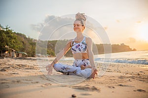 Beautiful woman practicing yoga on the beach. Sitting in Padmasana, Lotus Pose. Hands in gyan mudra. Closed eyes. Positive energy