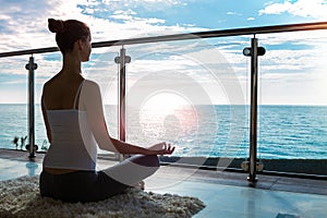 The beautiful woman practicing yoga on a rug and sitting on a balcony with the seaside view.